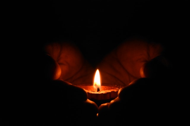 Človek drží v dlaniach zapálenú sviečku